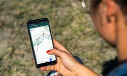 A smartphone displaying an overlanding GPS app mounted on the dashboard of a truck.