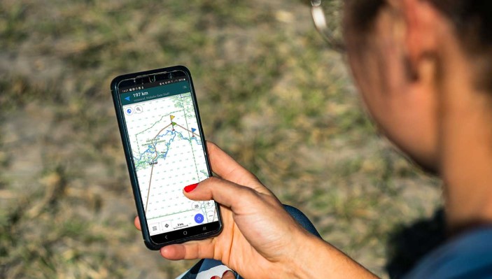 A smartphone displaying an overlanding GPS app mounted on the dashboard of a truck.