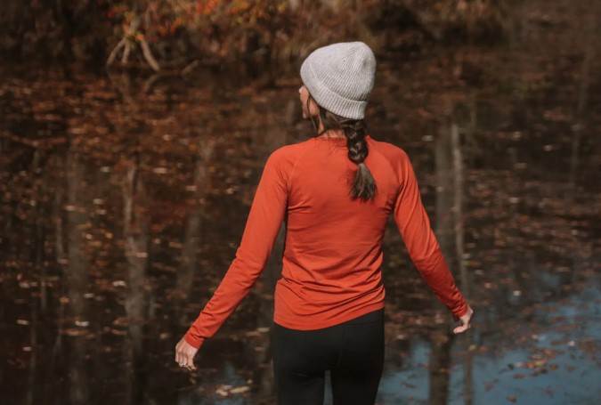 A camper wearing a Merino wool base layer sitting on the tailgate of a truck, drinking coffee on a cold morning.