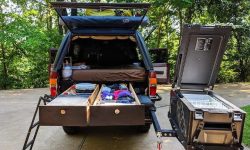 A custom wooden DIY truck bed sleeping platform with sliding storage drawers in the back of a pickup.