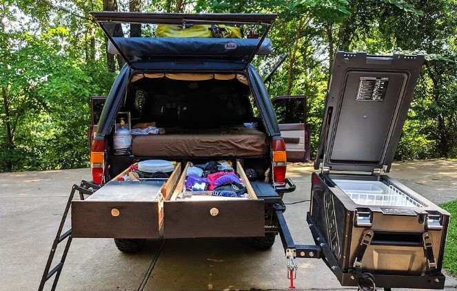 A custom wooden DIY truck bed sleeping platform with sliding storage drawers in the back of a pickup.
