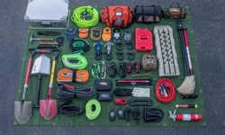 A tactical backpack and overlanding survival gear laid out on the tailgate of a truck.