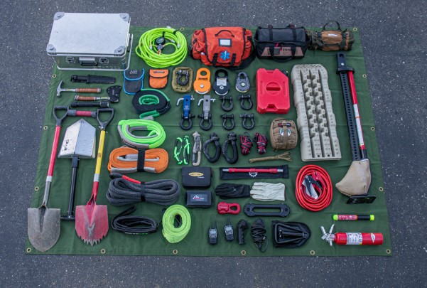 A tactical backpack and overlanding survival gear laid out on the tailgate of a truck.