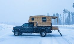 A truck parked in the snow with cozy, warm lighting glowing from the truck bed camper shell.